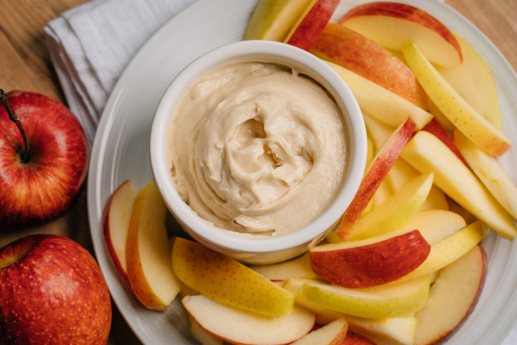 Creamy apple dip surrounded by slices of red and yellow apples.