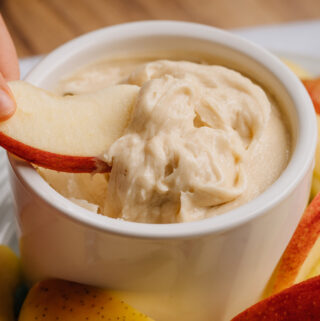Childs hand dipping a red apple slice into a creamy apple dip that takes just a couple ingredients to make.