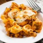 Creamy sausage tortellini with cheese topping on plate.