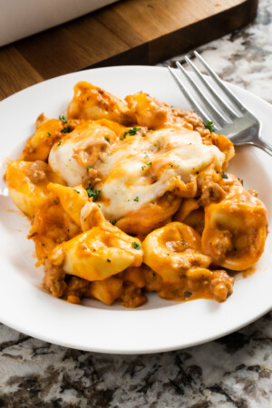 Creamy sausage tortellini with cheese topping on plate.