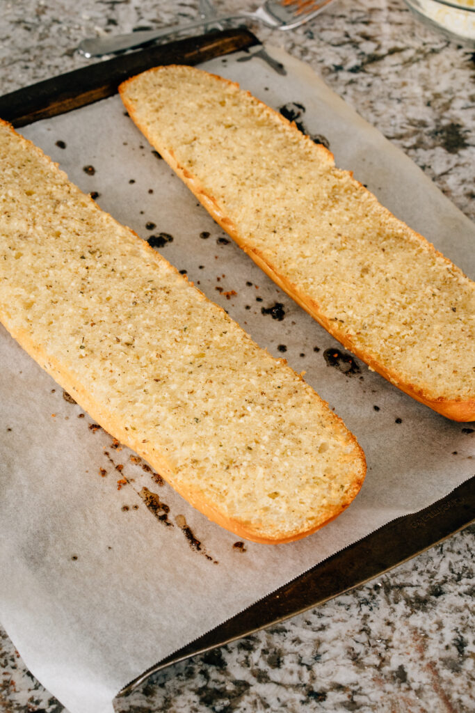 Toasted french bread coated in butter and garlic on a cookie sheet lined in parchment paper.