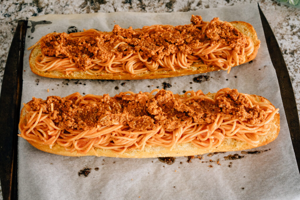 Toasted french bread coated in butter and garlic top with spaghetti and a meat sauce on a cookie sheet lined with parchment paper.