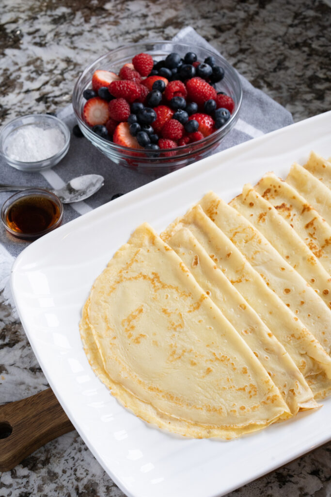 Soft and delicious crepes ready to be served. Fruit bowl with berries in background.