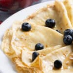 Close up of crepes folded drizzled in syrup and sprinkled with powdered sugar and blueberries ready to be served.