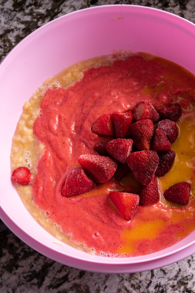 A giant bowl of frozen strawberries(some pureed), orange juice concentrate, crushed pineapple, and bananas read to be mixed up into fruit freeze ups.