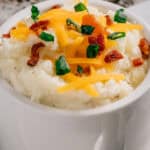 Close up of loaded mashed potatoes that has cream cheese and butter in them and topped with cheddar cheese and green onions.