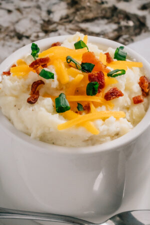 Close up of loaded mashed potatoes that has cream cheese and butter in them and topped with cheddar cheese and green onions.