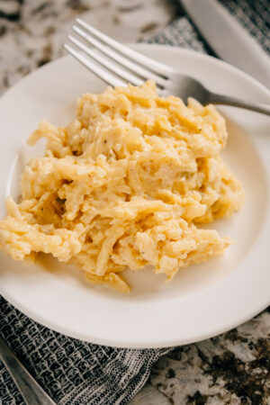 A single serving of creamy party potatoes made with sour cream, cream of celery soup, cheddar cheese and hash browns plated.