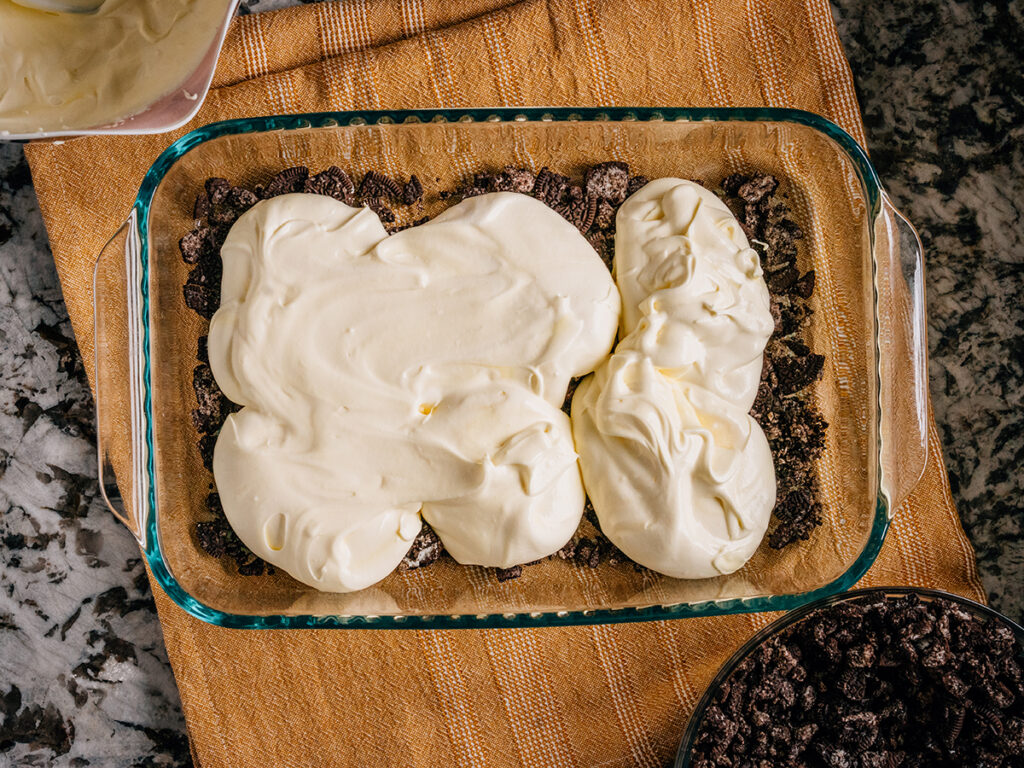 Step 2: Add a layer of the cream cheese, vanilla pudding and whipped topping mixture on top of the crushed Oreos.
