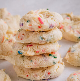 Five cake cookies with sprinkles baked in them stacked up surrounded by others all around.