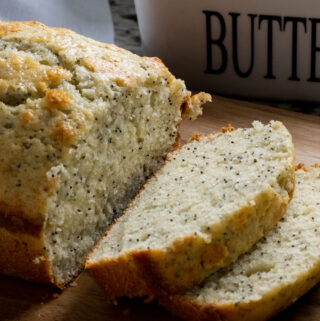 Lemon poppy seed bread sliced with a few pieces laying open on a cutting board in front of a butter dish.