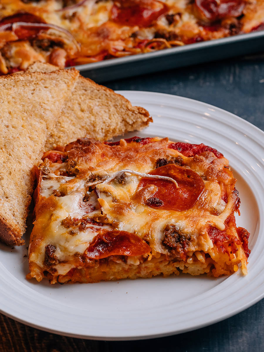 This photo shows a plate with a square serving of Pizza Spaghetti Bake with a side toast. 