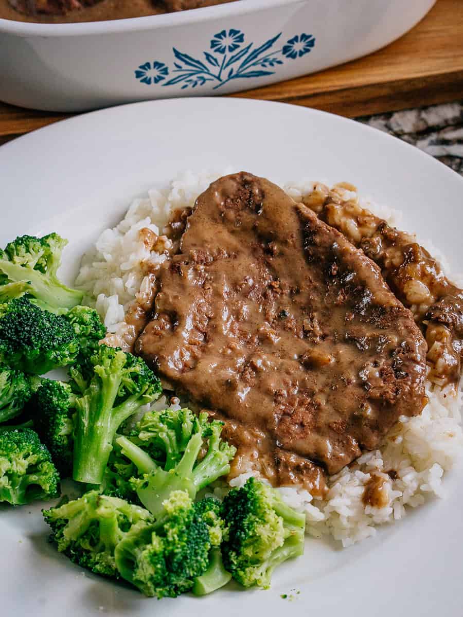 This is a photo showing a piece of slow cooker cube steak served over a bed of white rice with a side of broccoli. 