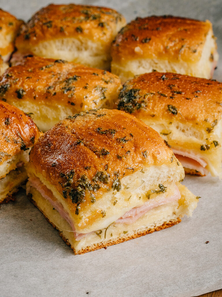 Ham and cheese sliders straight from the oven. Gooey cheese and delicious ham on toasted Hawaiian rolls brushed with a flavorful butter mixture!