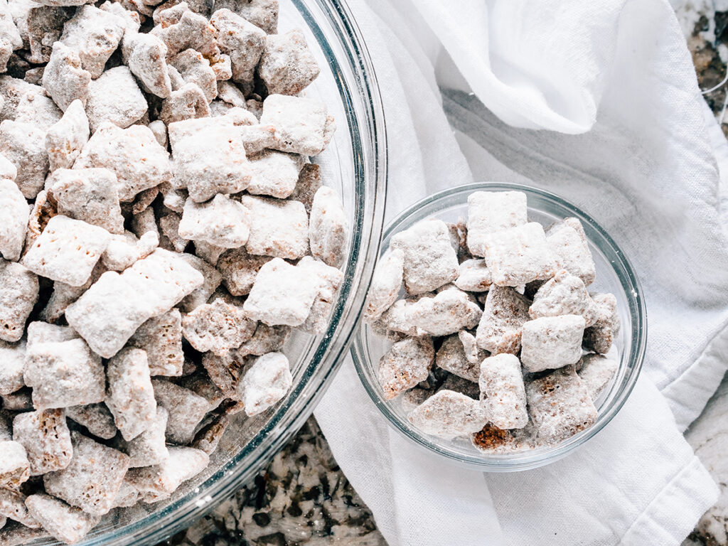 A bowl of crunchy chocolate and sugar delight: puppy chow! Overview shot one small bowl beside the party bowl.