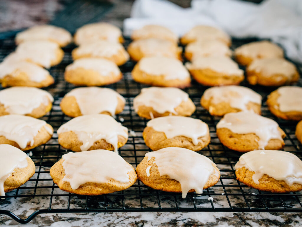 Freshly baked and glazed pumpkin cookies on a black cooling rack.