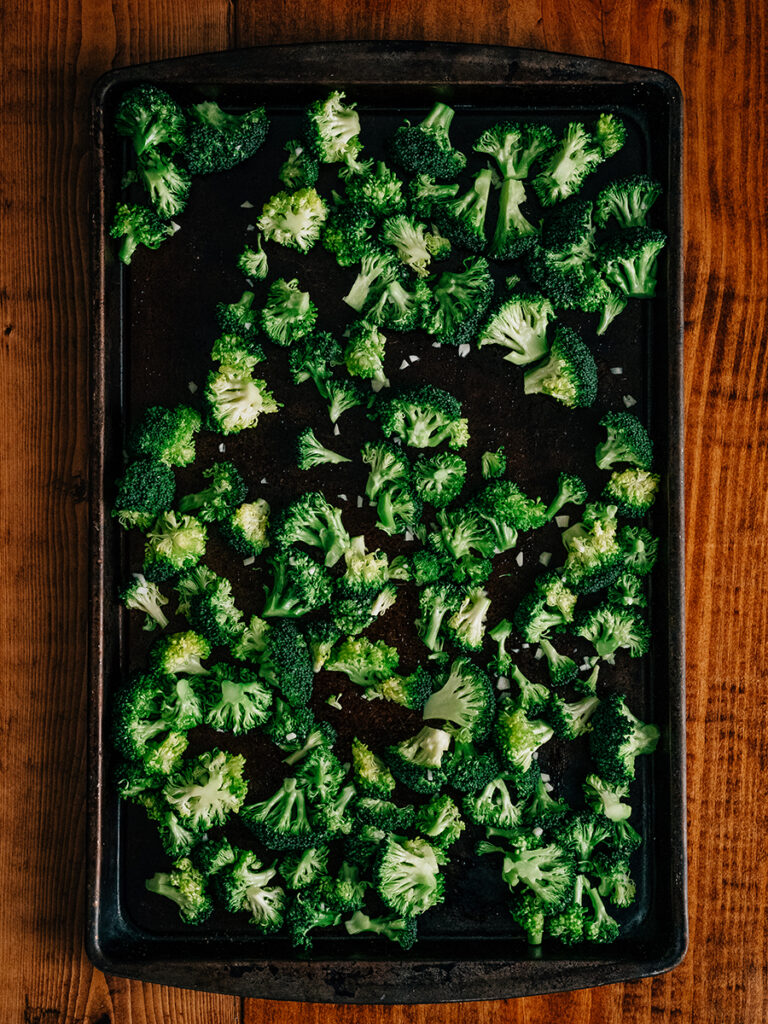 Fresh broccoli florets cut to the same size and toss with oil, lemon juice, minced garlic and salt spread out on a baking sheet ready for roasting.