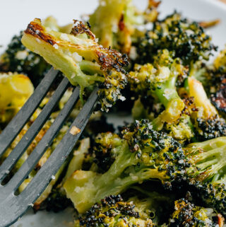 A piece of tender roasted broccoli with parmesan speared by a fork, warm, flavorful, and ready to eat!