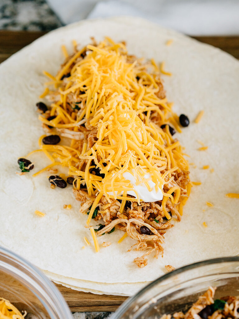 A southwest chicken wrap laying open, ready to be folded, and then grilled to a crisp. Add more sour cream and shredded cheese.