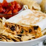 A crispy southwest chicken wrap with a couple of bites taken out of it laying on a bed of tortilla chips with salsa in the background.