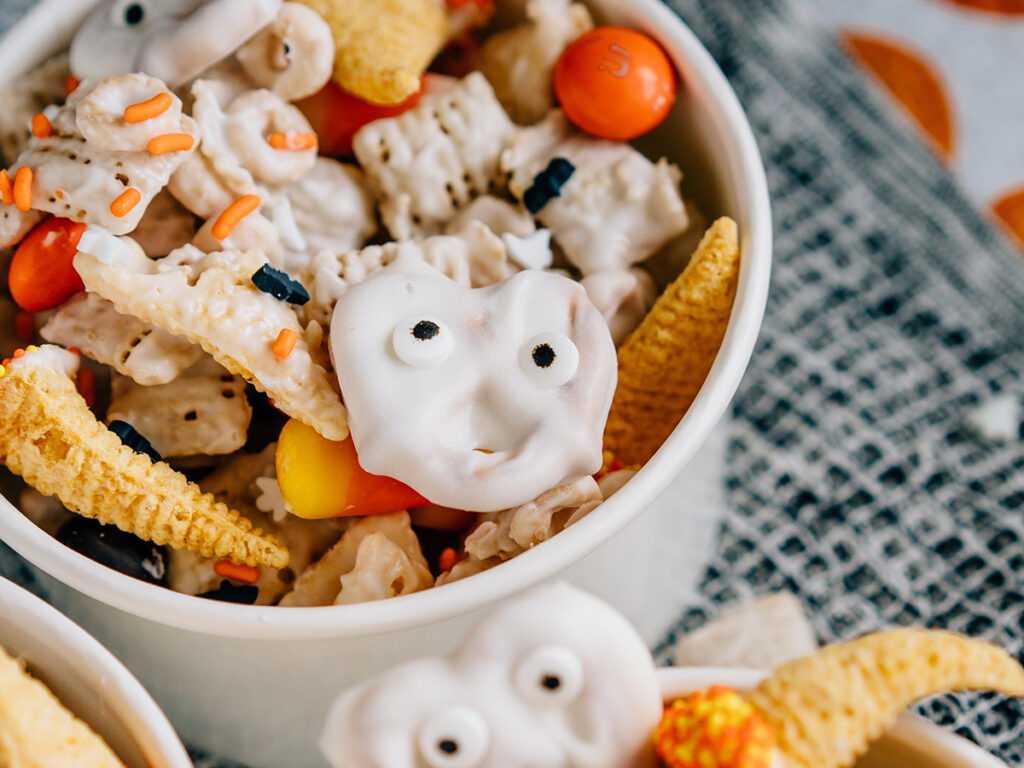 Ghost faces and witches hats mixed with a seasonal white trash mix make this ultimate Halloween party mix spooktacular. Here it is served in ice cream bowls getting for guests!