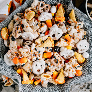 Ghost faces and witches hats mixed with a seasonal white trash mix make this ultimate Halloween party mix spooktacular. Here it is served in a large bowl ready for guests!