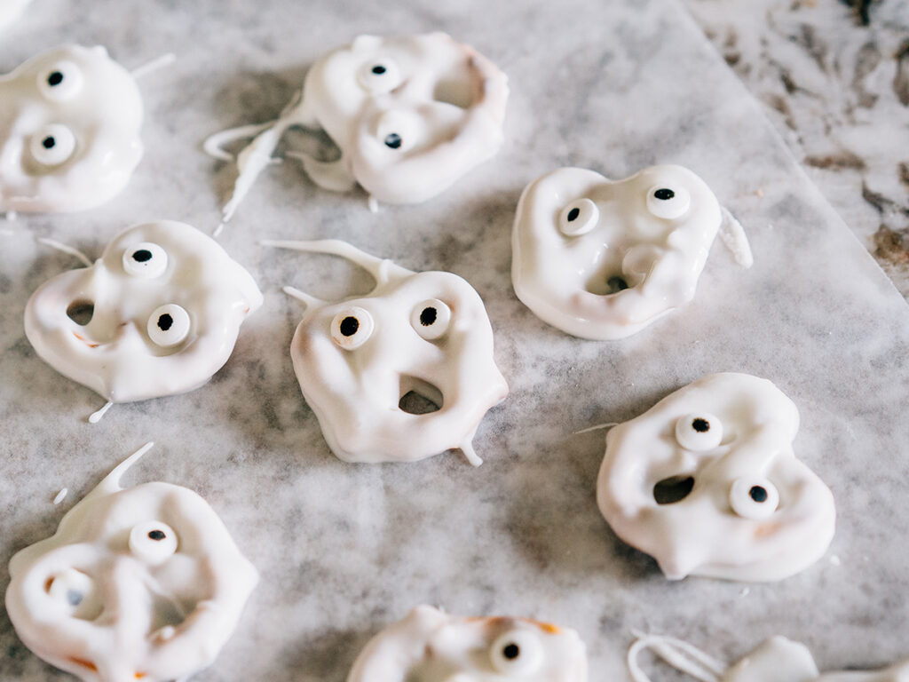 Hilarious ghost faces are yummy white chocolate covered twisted pretzels with candy eyes laying on wax paper.