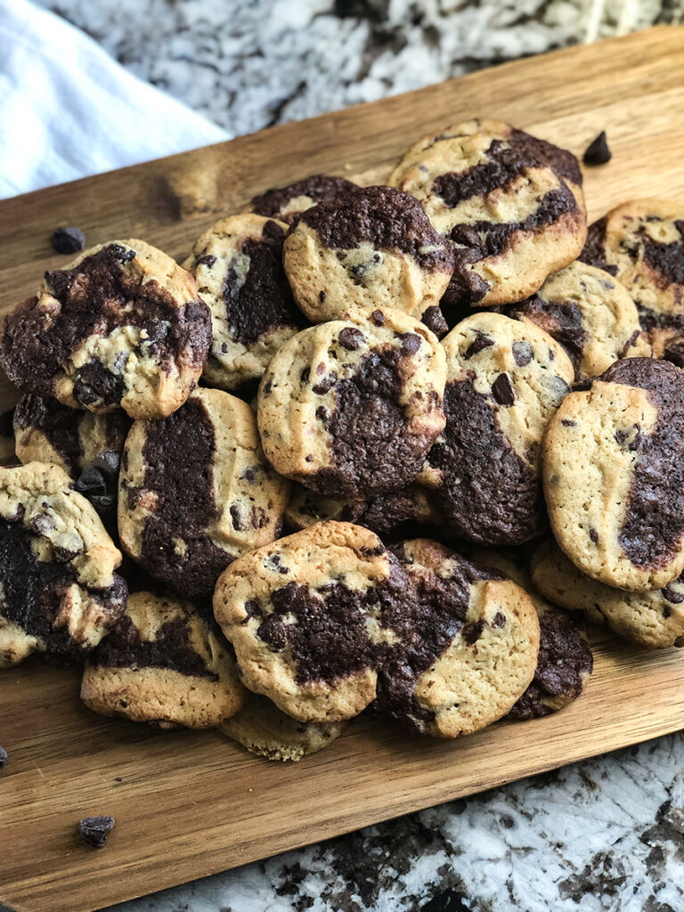 Pile of delicious Brookie Cookies on a cutting board with chocolate chips scattered in front wide angle view.
