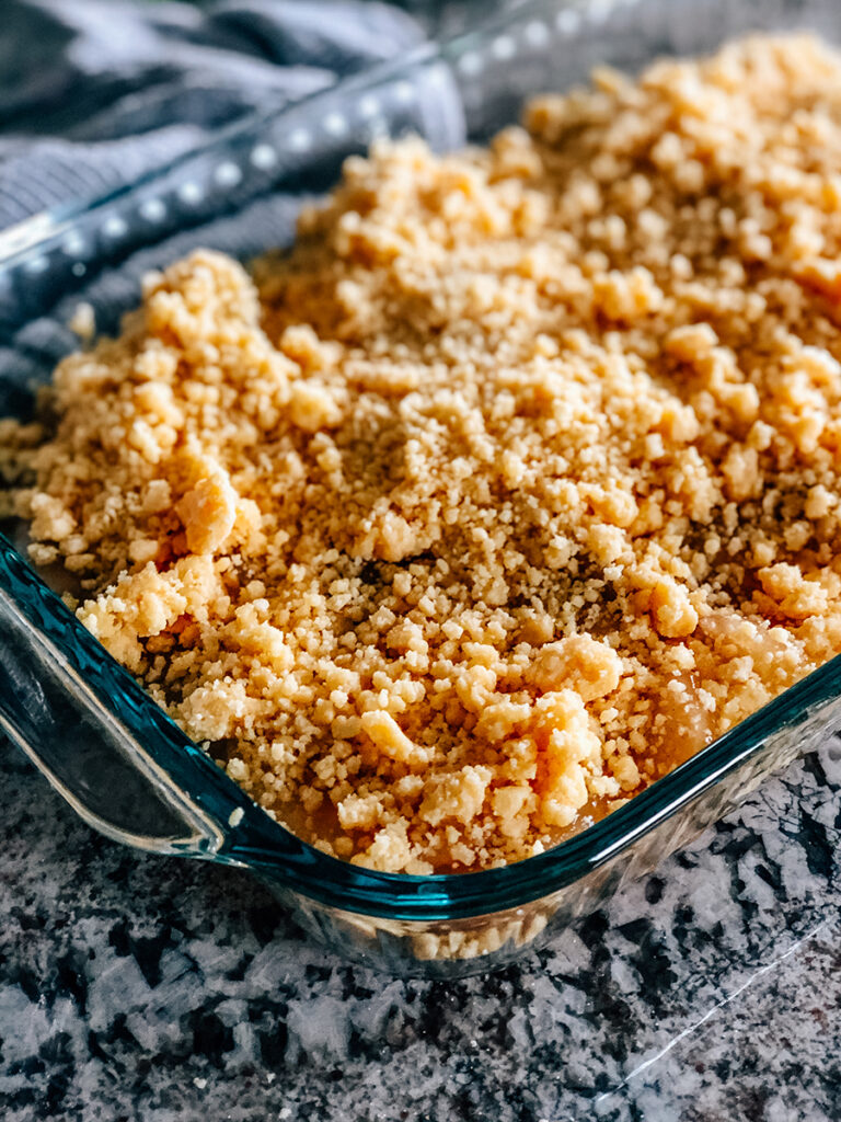The butter and yellow cake mix crumble add to the pan on top of the apple pie filling and caramel syrup.