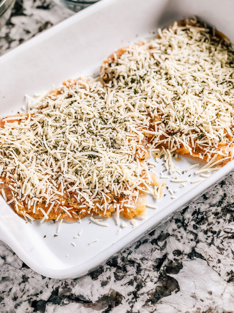 Raw chicken topped with a garlic marinade and parmesan cheese topping in a baking dish ready to be put in the oven.