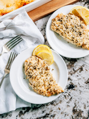A plated and sliced baked garlic parmesan chicken breast with lemon slices on the side.