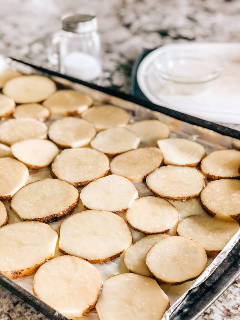 Potato slices side by side on a baking sheet lined in foil and covered in melted butter.