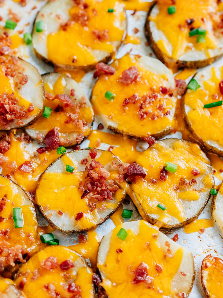 Load baked potato slices topped with melted cheddar cheese, savory bacon bits and green onion side by side on a baking sheet.