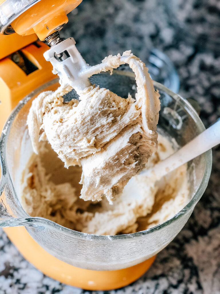 The beater of a stand mixer covered in creamed together butter, sugar and eggs. The first step of making sugar cookie dough.