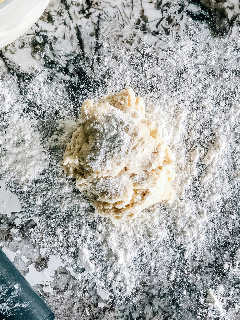 A ball of cooled sugar cookie dough sprinkled with flour ready to be rolled out.