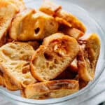 Side view of toasted baguette slices with garlic in a glass bowl.