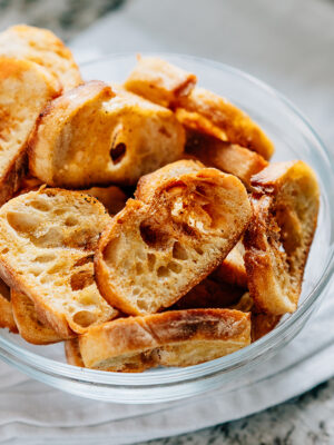 Side view of toasted baguette slices with garlic in a glass bowl.