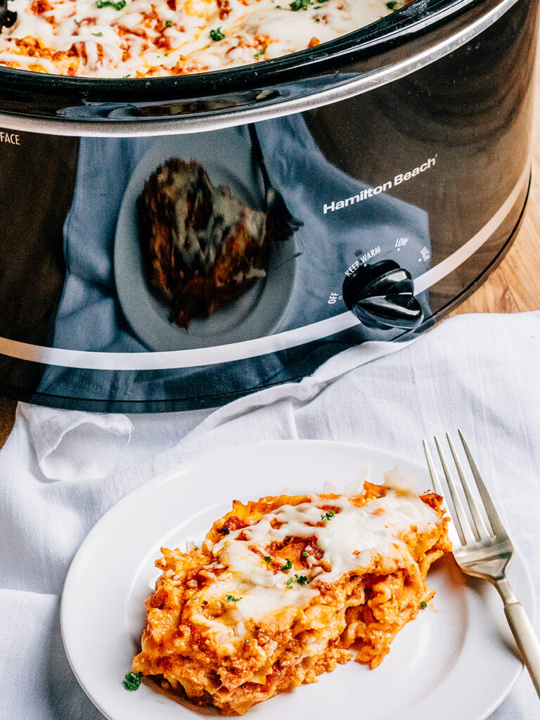 A serving of easy crockpot lasagna plated and ready to eat with the crockpot in the background.