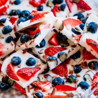 A stack of frozen yogurt bars with strawberries and blueberries on parchment paper.
