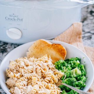 A shot of the crock pot garlic parmesan chicken pasta meal with steamed broccoli and garlic toast sitting in front of the crockpot.