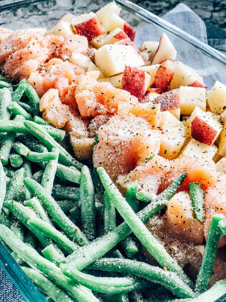An Italian salad dressing packet sprinkled on top of the raw chicken breast, cubed red potatoes, and frozen green beans.