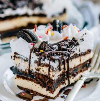A close of view of this Oreo Fudge Ice Cream Cake with a oreo and hot fudge layer between two layers of vanilla ice cream sandwiches then topped with cool whip, mini oreos, more crushed oreos, and a drizzle of magic shell chocolate topping. Yum!