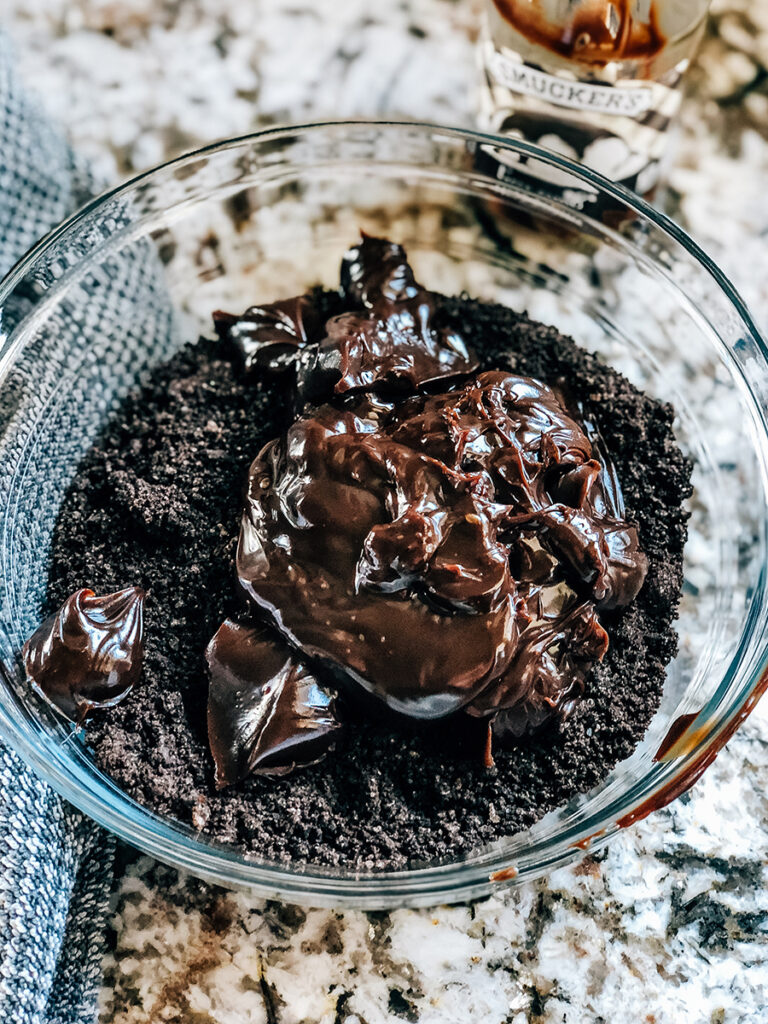 The slightly warmed hot fudge topping on top of the crushed oreos in a glass bowl.