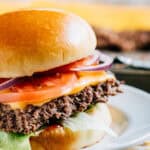 Close up of a sheet pan hamburger on a bun topped with cheese, ketchup, lettuce, tomato, and red onion.