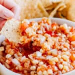 A tortilla chip dipped with pineapple corn salsa showing off the chunky salsa, corn, pineapple, and chopped sweet onion.