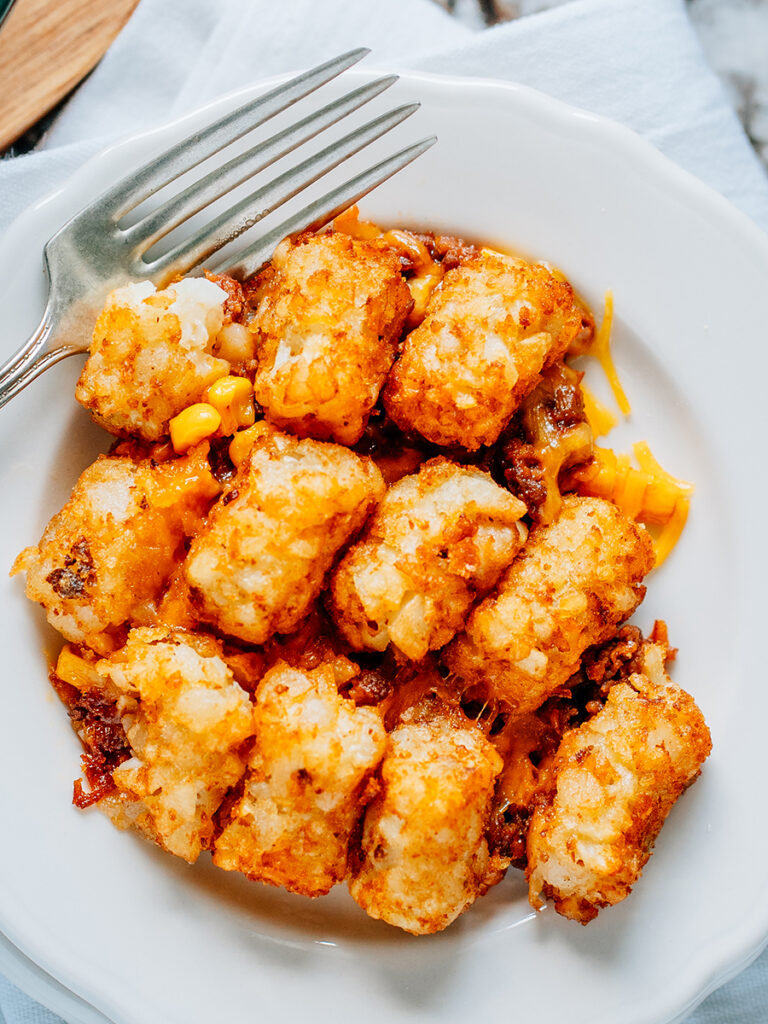 Overview of a plate of tater tot casserole made from sloppy joe, shredded cheese and corn.