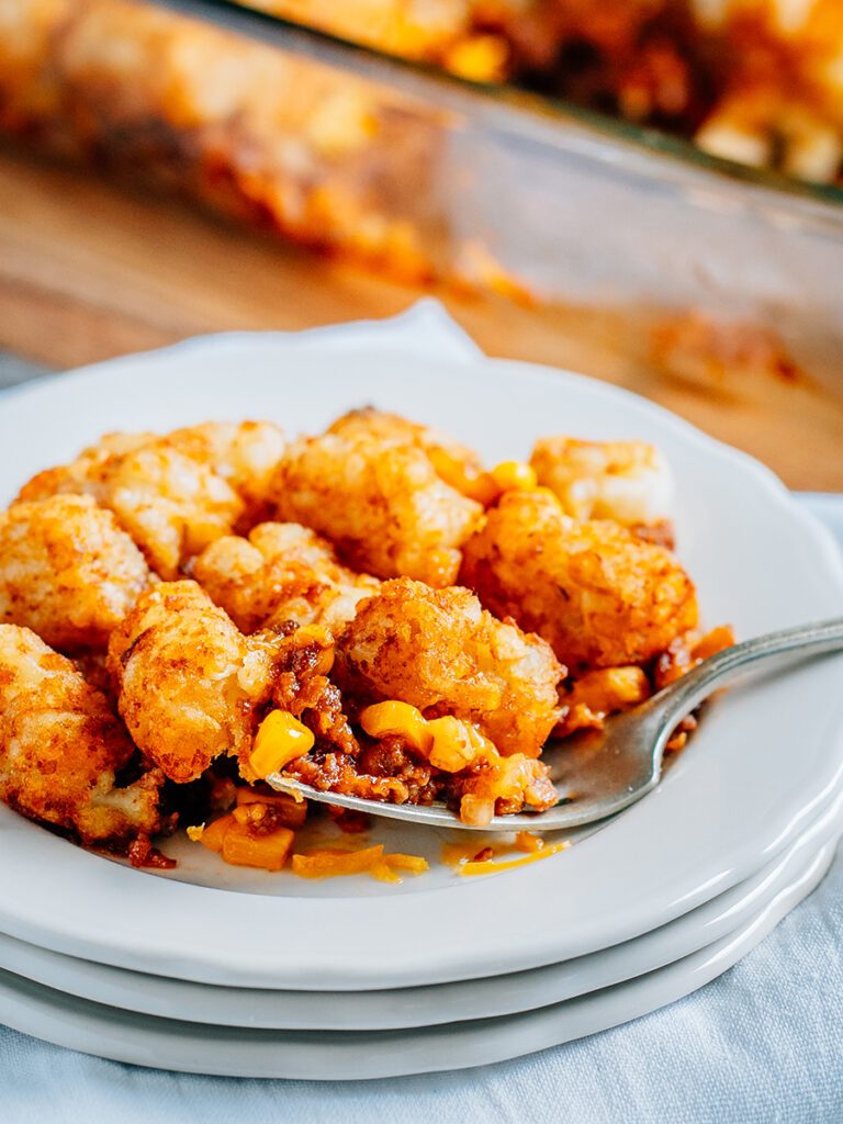 A fork full of sloppy joe tater tot casserole on a plate showing off the sweet sloppy joe, gooey melted cheese, and crisp tater tots.