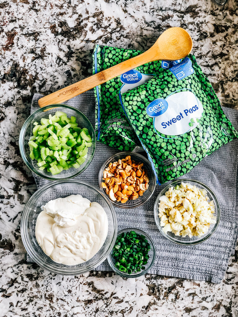 The ingredients for Crunchy Pea Salad with Cashews: frozen peas, chopped cauliflower and cashews, diced celery and green onion, and a homemade dressing of ranch and sour cream.