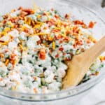 Crunchy pea salad with cashews covered in a homemade ranch and sour cream dressing and garnished with bacon bits and shredded cheddar cheese in a serving bowl. Ready to eat.