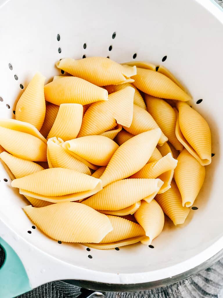 Cooked, drained and cooled jumbo pasta shells in a strainer.